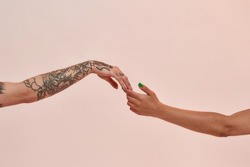 Closeup of two female arms reaching each other hand isolated over light pink background. Lgbtq, youth, love concept
