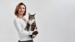European woman holding furry Maine Coon cat in hands. Concept of relationship between human and animal. Idea of owner and pet friendship. Lady and furry cat on white background in studio. Copy space