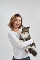 Adult caucasian woman holding furry Maine Coon cat in hands. Concept of relationship between human and animal. Idea of owner and pet friendship. Lady and furry cat on white background in studio