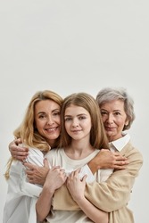 Caucasian family of grandmother, mother and granddaughter hugging and looking at camera. Age and generation concept. Family relationship and closeness. White background. Studio shoot. Copy space