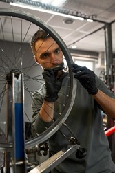 Cycling mechanic or technician checking bicycle wheel spoke with bike spoke key in modern blurred workshop. Young concentrated caucasian bearded man. Bike service, repair and upgrade
