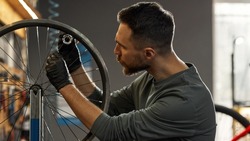 Cycling serviceman checking bicycle wheel spoke with bike spoke key in modern workshop. Young caucasian bearded man. Bike service, repair and upgrade. Garage interior with tools and equipment