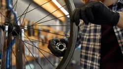 Partial image of male cycling repairman checking bicycle wheel spoke with bike spoke key in modern workshop. Bike service, repair and upgrade. Garage interior with tools and equipment