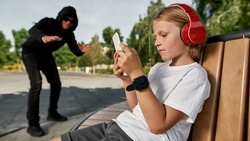 Focus on foreground of lonely boy browsing smartphone on bench on background of sly pedophile or kidnapper on playground outdoors. Digital generation alpha. Gadget addiction. Childhood lifestyle