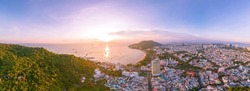 Vung Tau city aerial view with beautiful sunset and so many boats. Panoramic coastal Vung Tau view from above, with waves, coastline, streets, coconut trees and Tao Phung mountain in Vietnam.