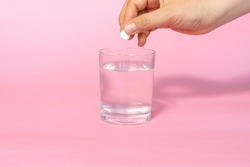 woman's hand throws a pill into a glass of water, pink background