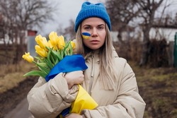 Portrait of sad Ukrainian woman holding tulip flowers with Ukrainian flag. War between Russia and Ukraine.