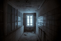 Dark corridor with a window. An old room in an abandoned building. Light from the window. Scary atmosphere. An old abandoned building. The interior of an abandoned house. Tiles on shabby walls.