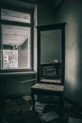 An old broken mirror stands in an abandoned building. Wooden mirror. Dirty and shabby walls. The depressing atmosphere of an abandoned building. Light from the window.