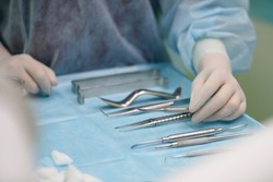 Surgical instruments in the operating room. A nurse in a surgical suit and gloves is preparing for a tooth implant operation.
Dental probe, tweezers, scalpel, needle holder, rasps on instrument table.