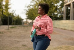 Overweight curly african american female with a bottle of water in a public park at sunset