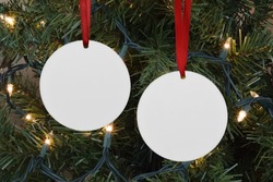 Closeup of two round Christmas Ornaments hanging merrily from a lit up Christmas tree.