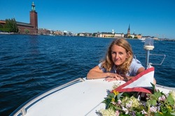 Stockholm, Sweden A woman celebrates midsummer on a boat on the water with the City Hall in background.
