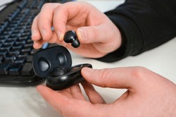 Wireless headphones. Small comfortable wireless black headphones with case in male hands above keyboard of computer.