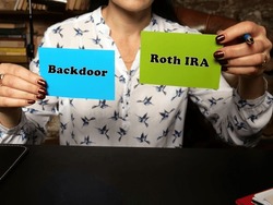 Woman's hand showing green and blue business cards with phrase Backdoor Roth IRA - closeup shot on grey background