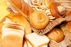 Culinary background with bread,buns,drying bagels,wheat ears in a wicker basket, on yellow