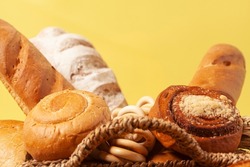 Culinary background with bread,buns,drying bagels,wheat ears in a wicker basket, on yellow