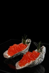 Red caviar is found in oyster shells. Serving snacks with red caviar. A symbol of wealth. A useful omega. Black background. Space for copying. Vertical photo.