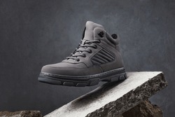 Male walking boots with stones or concrete block on gray background. Autumn stylish leather shoes for adventure or travel.