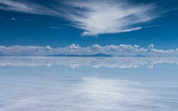Mirror effect in Uyuni salt flat, Bolivia, with mountains and clouds in the view