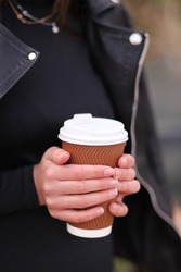 Close-up of female hands holding a large plastic disposable cup with coffee, cappuccino. Vertical Orientation