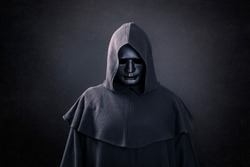 Scary figure with mask in hooded cloak in the dark