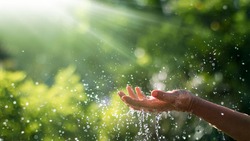 Water pouring and splash in woman hand on nature background, earth day, environment issues 