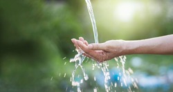 Water pouring in woman hand on nature background, environment issues