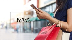 Black Friday, Woman using smartphone and holding shopping bag while standing on the mall background