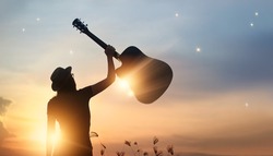 Musician holding guitar in hand of silhouette on sunset nature background