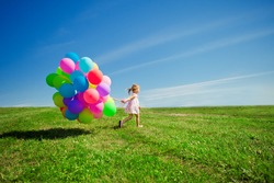 Happy little girl holding colorful balloons. Child playing on a green meadow. Smiling  kid. 