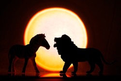 Zebra and lion silhouette. African animals. Predator and prey against the backdrop of the sun. Hunting in the wild world against the backdrop of sunset or dawn