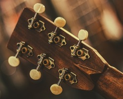 The neck of an acoustic guitar with a close-up tuning mechanism. The neck of the acoustic guitar is made of natural wood in close-up. Guitar tuning pegs.