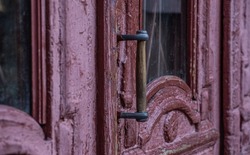 The handle of an old wooden door. Selective focus. Antique door with cracked paint and wooden handle close-up. Vintage entrance door with glass inserts.Old rusty door handle. 