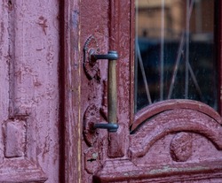 The handle of an old wooden door. Selective focus. Antique door with cracked paint and wooden handle close-up. Vintage entrance door with glass inserts.Old rusty door handle. 