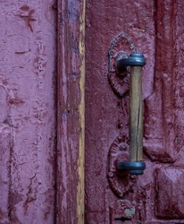 The handle of an old wooden door. Selective focus. Antique door with cracked paint and wooden handle close-up. Vintage entrance door with glass inserts.Old rusty door handle. Vertical photo. 