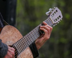 Wrinkled hands of an adult man playing an acoustic guitar on the street, in a park close-up, selective focus. A man is playing an old acoustic guitar on the street. A street musician. Composer.