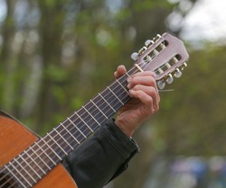 Hands of an adult man playing an acoustic guitar on the street, in a park close-up, selective focus. A man is playing an old acoustic guitar on the street. A street musician. Composer.Spanish guitar.