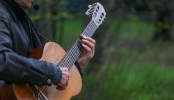 Hands of an adult man playing an acoustic guitar on the street, in a park close-up, selective focus. A man is playing an old acoustic guitar on the street. A street musician. Composer.Spanish guitar.