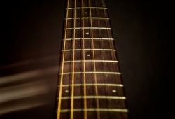 The neck of a six-string acoustic guitar on a dark background is a selective focus.  Isolated guitar neck on a dark background. Wooden neck of a 6-string acoustic guitar. Guitar fingerboard. 