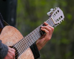 Hands of an adult man playing an acoustic guitar on the street, in a park close-up, selective focus. A man is playing an old acoustic guitar on the street. A street musician. Composer.	