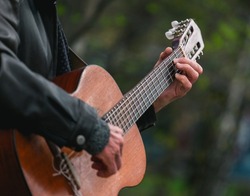 Hands of an adult man playing an acoustic guitar on the street, in a park close-up, selective focus. A man is playing an old acoustic guitar on the street. A street musician. Composer.	