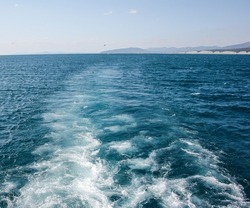 A foamy trail on the sea from the ship's propellers. The foamy path behind the stern of the ship with a view of the coast is a selective focus. The concept of a summer sea holiday.Seascape background.