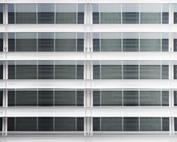 Perforated shutters over glass panels. Material background of steel or aluminum resembling hi-tech architecture or modern industrial building fragment. Geometric composition of parallel lines.