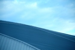 Abstract architecture of modern building. Corrugated metal roof of hangar, warehouse, repository or stock house. Close-up photo of industrial real estate object. Geometric structure of parallel lines.