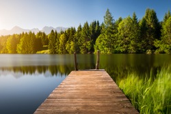 Idyllic view of the wooden pier in the lake with mountain scenery background. Alps in the early morning.