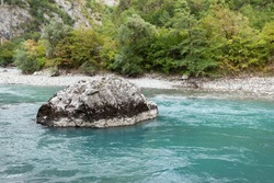 Turquoise mountain river, in the center of the river lies a large light stone, in the background a bank with dense vegetation, used as a background or texture