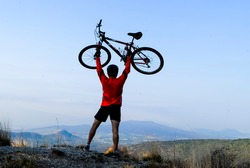 Male cyclist celebrating with his bike in his arms in high gear conquering the mountain