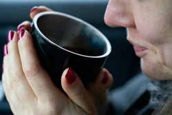 Young woman sits in the trunk of the car and holds a cup of hot drink in her hands