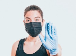 Young woman wearing protective mask on face and medical gloves. Showing stop sign. Confident girl, female doctor in medical mask and protective gloves. Coronavirus COVID-19 protection.